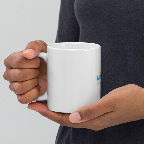 Person holding white mug with logo.